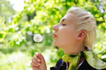 Close-up portrait of a woman blowing to dandelion flowerの写真素材