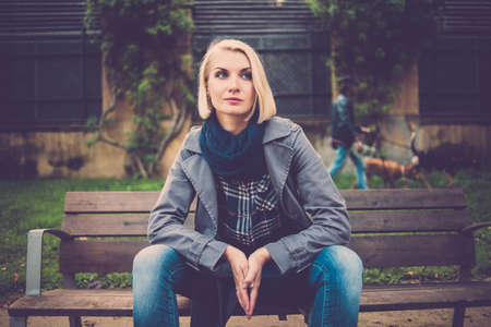Beautiful pensive blond woman sitting on bench in park outdoorsの写真素材