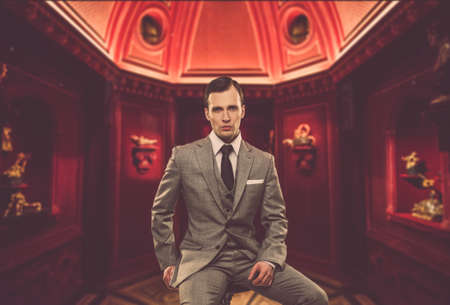 Confident man in classic grey suit sitting on chair in cabinetの写真素材