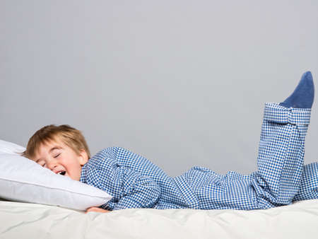 Playful little boy wearing blue pyjamas in bedの写真素材
