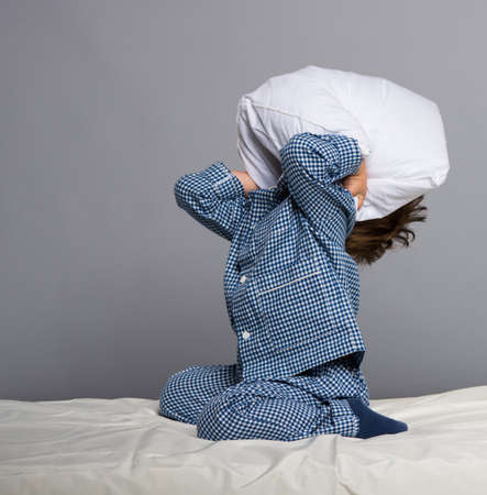 Playful little boy wearing blue pyjamas in bedの写真素材