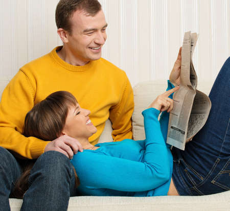 Happy young man and woman with newspaper on sofa in home interiorの写真素材
