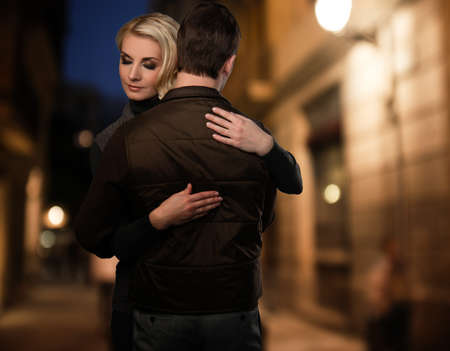 Blond woman embracing man in brown vest outdoors at night