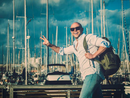 Happy middle-aged man with backpack against yacht port