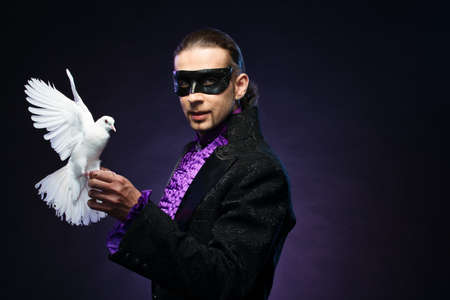 Young handsome brunette magician man in stage costume with his trained white doveの写真素材
