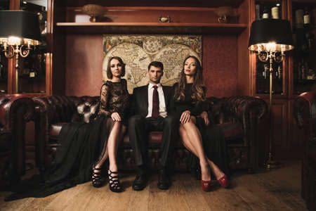 Handsome brunette wearing suit sitting on sofa with two beautiful women の写真素材