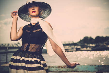 Woman in white hat and scarf standing near old pier rails の写真素材