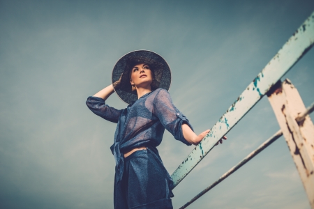 Stylish woman in white hat standing near rails of old pierの写真素材