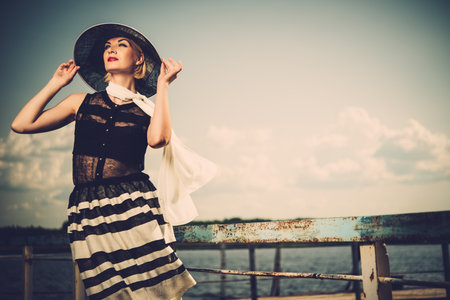 Woman in white hat and scarf standing near old pier rails の写真素材