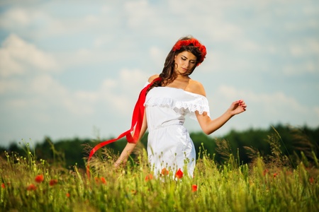 Beautiful young brunette girl wearing white summer dress and flower chaplet in poppy filedの写真素材
