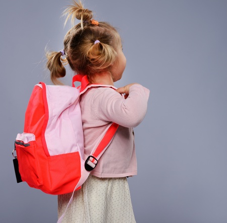 Funny little school girl with a backpack isolated on grey の写真素材