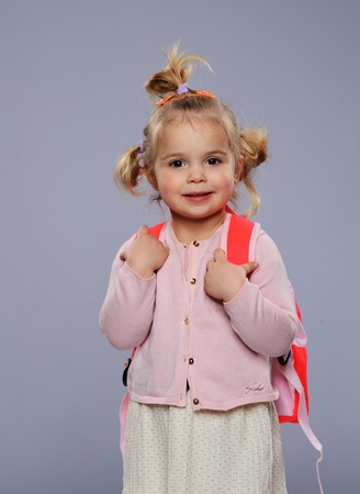 Funny little school girl with a backpack isolated on grey の写真素材