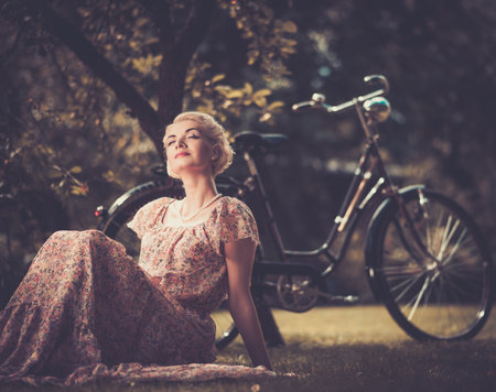 Dreaming blond retro woman in summer dress sitting on a meadowの写真素材