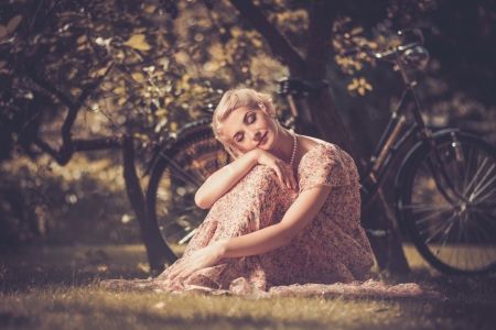 Dreaming blond retro woman in summer dress sitting on a meadowの写真素材