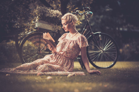 Blond beautiful retro woman reading book on a meadow の写真素材