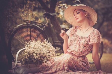 Beautiful retro woman with basket of flowers n and bicycle behind herの写真素材