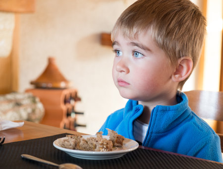 Grievous little boy sitting behind table with full plateの写真素材