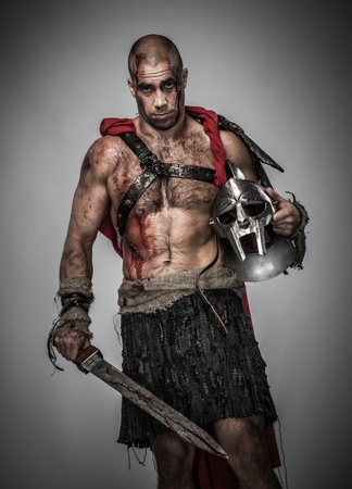Wounded gladiator with sword covered in blood and helmet isolated on greyの写真素材