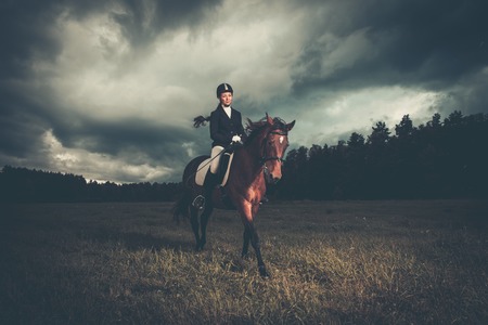 Beautiful girl sitting on a horse outdoors against moody skyの写真素材