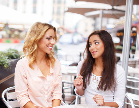 Two beautiful girls chatting in summer cafe の写真素材
