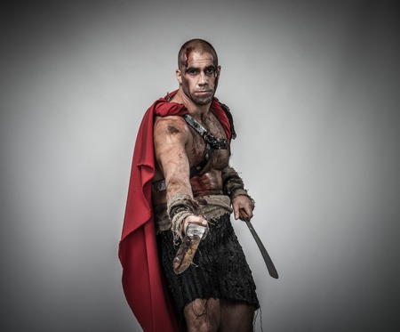 Wounded gladiator with sword covered in blood isolated on greyの写真素材