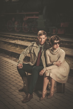 Beautiful vintage style couple sitting on suitcases on  train station platform