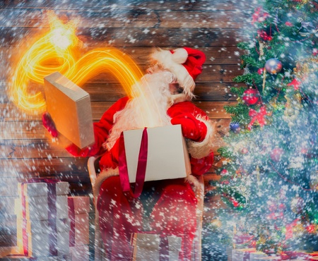 Santa Claus in wooden home interior holding gift box with magic star flying out of it の写真素材