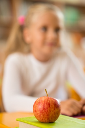 Apple in front of little schoolgirl sitting behind school desk during lesson in schoolの写真素材