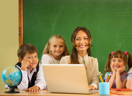 Group of happy classmates with their teacher in class near blackboard 