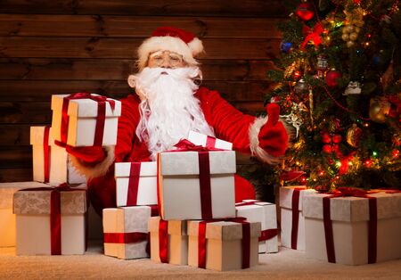 Santa Claus sitting on a carpet  in wooden home interior with gift boxes around him の写真素材