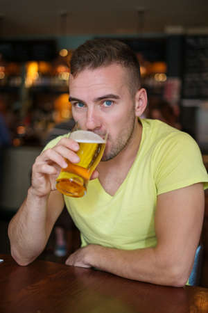 Handsome young man drinking light beer in a pubの写真素材