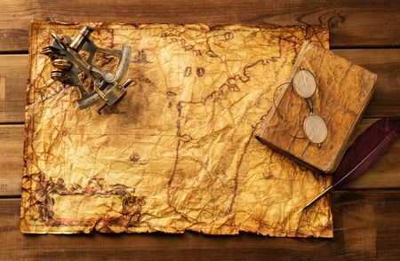Sextant, old book and glasses on vintage map over wooden 