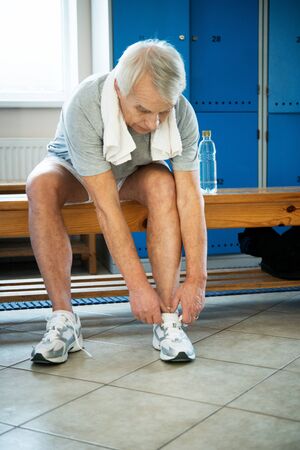 Senior man tying up sneakers in fitness club locker roomの写真素材