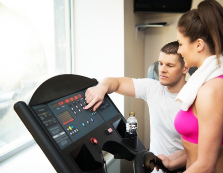 Trainer explains to a young woman how to use treadmill in fitness club