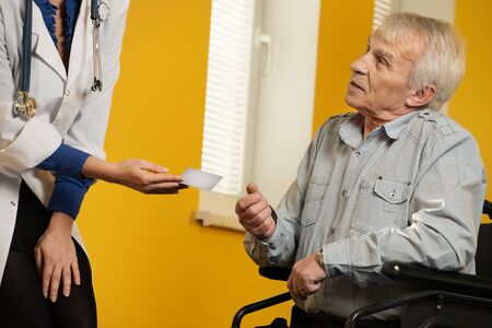 Nurse woman giving client card to senior man in wheelchair の写真素材