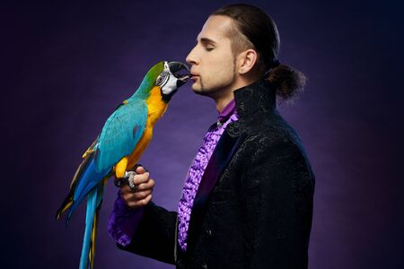 Young handsome brunette magician man in stage costume with his trained parrotの写真素材
