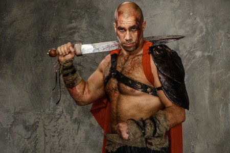 Wounded gladiator with  sword covered in blood isolated on greyの写真素材