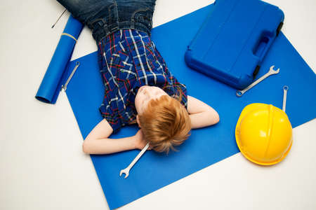 Funny little mechanic boy with wrench tools lying on a blueprint 