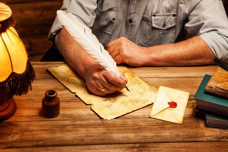 Senior writing letter with quill pen in homely wooden interior の写真素材