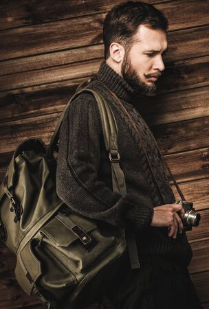 Handsome man wearing cardigan with backpack and vintage camera in house interior の写真素材