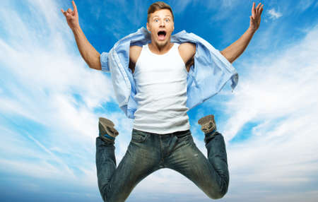 Funny man in blue shirt and jeans jumping against blue sky