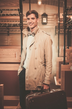 Handsome young man with suitcase in coat inside vintage train coach の写真素材