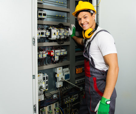 Cheerful electrician in a safety hat on a factoryの写真素材