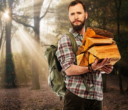 Handsome traveler with backpack and logs for bonfire  in autumnal forest の写真素材