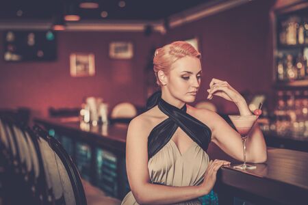 Beautiful blond woman in evening dress sitting near bar counterの写真素材
