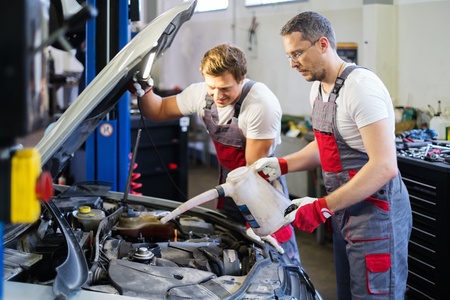 Two mechanics adding oil level in a car workshopの写真素材