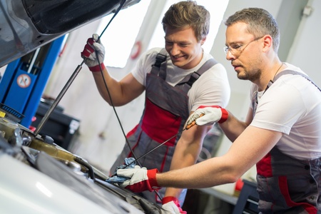 Two mechanics checking oil level in a car workshop