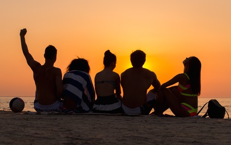 Silhouettes a young people sitting on a beach looking at  sunset の写真素材