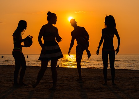 Silhouettes a young people having fun on a beach against sunset の写真素材