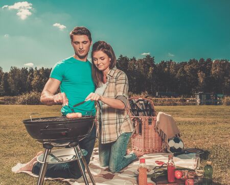 Young couple preparing sausages on a grill outdoors の写真素材